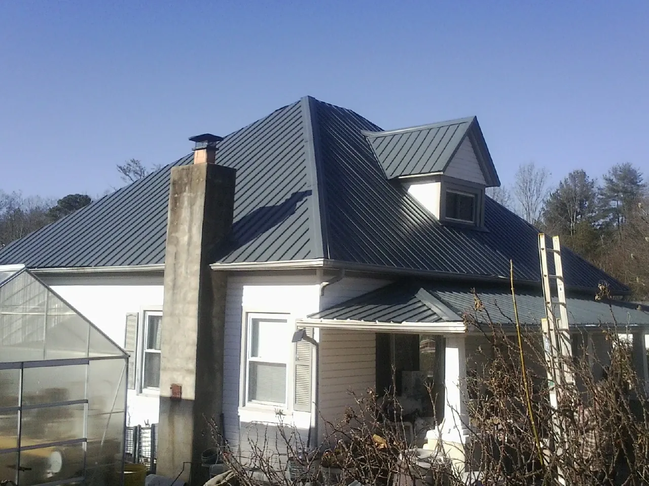 Dark blue standing seam metal roof on a white farmhouse with dormer in Rock Island