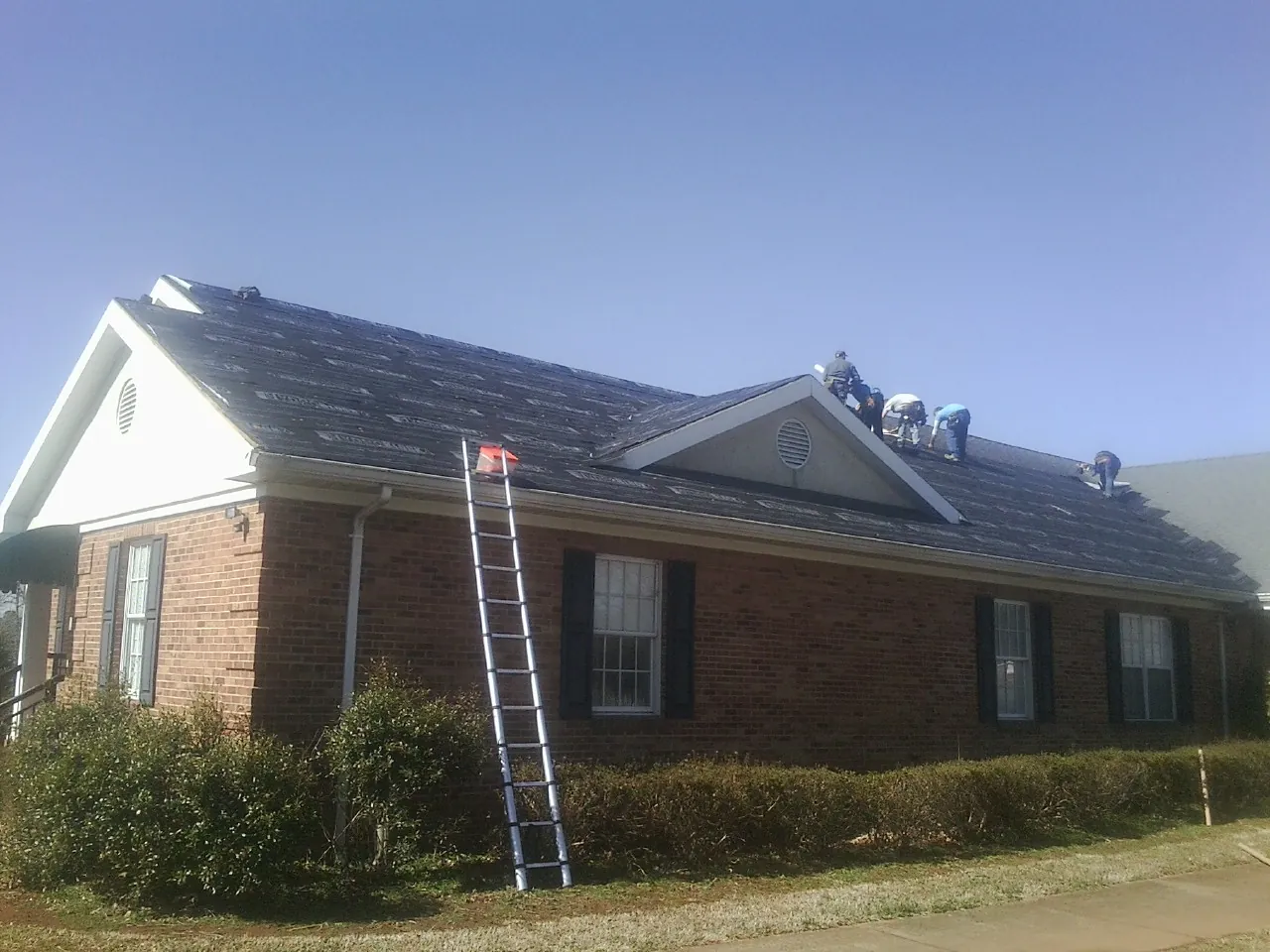 Crew tearing shingles off a brick ranch roof with a ladder set — Emergency Roof Repair work by our crew in Rock Island