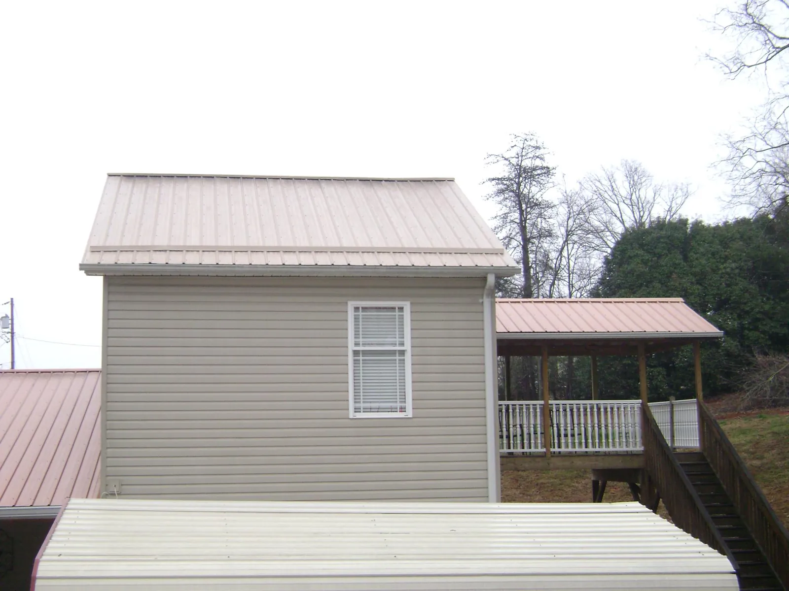 Tan metal roofs on a two story addition and attached porch, from a Roof Replacement job in Rock Island